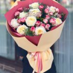 Букет для мамы из 9 крупных белых роз, веток кустовой бело-розовой розы и зеленью в матовой бежево-бордовой упаковке.